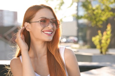 Beautiful smiling woman in sunglasses on city street, space for text