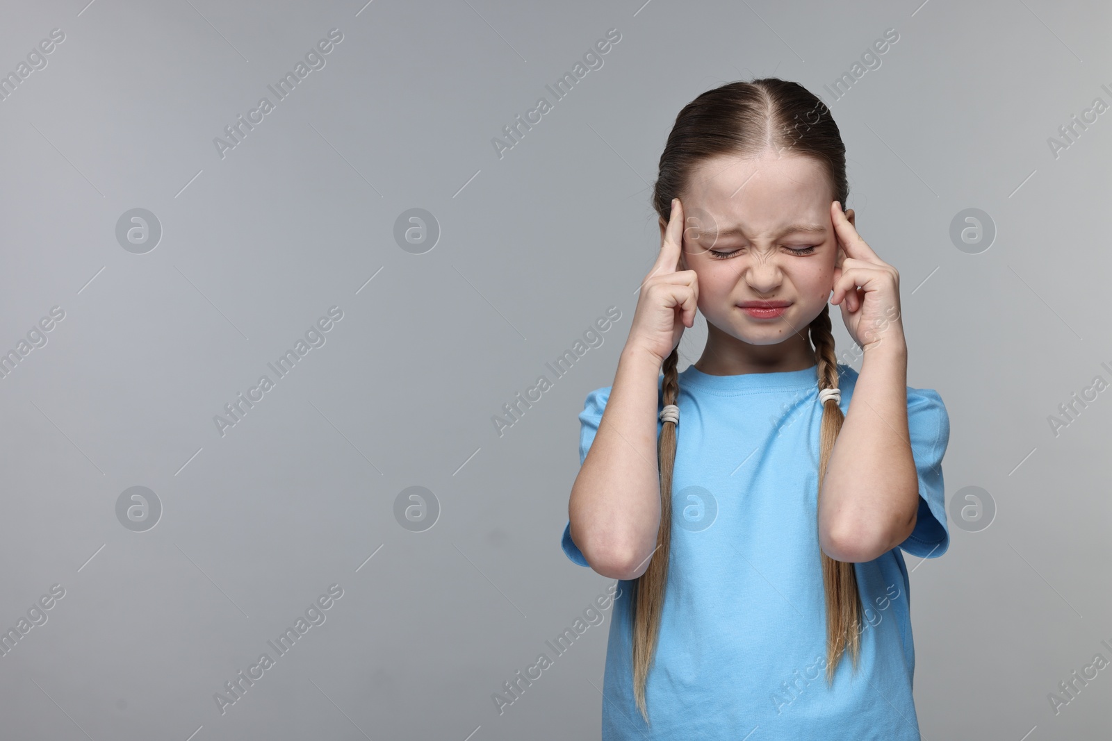 Photo of Little girl suffering from headache on grey background. Space for text