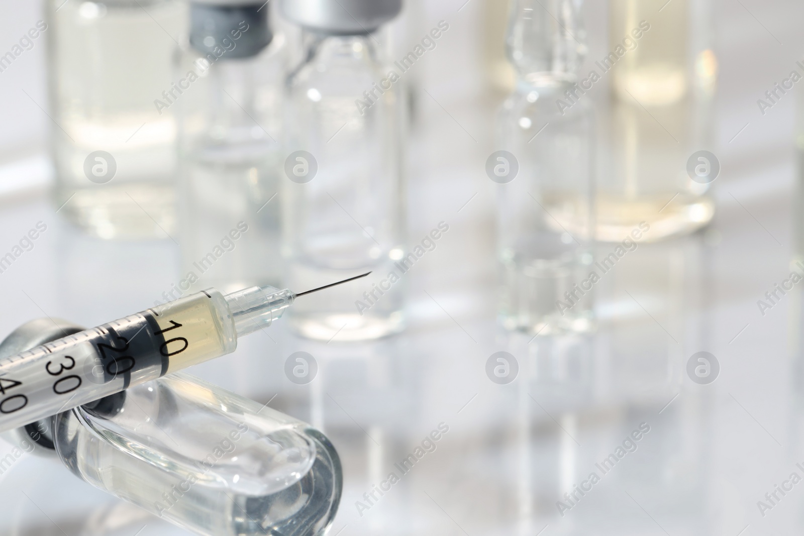 Photo of Glass vial and syringe with medication on white table, closeup. Space for text