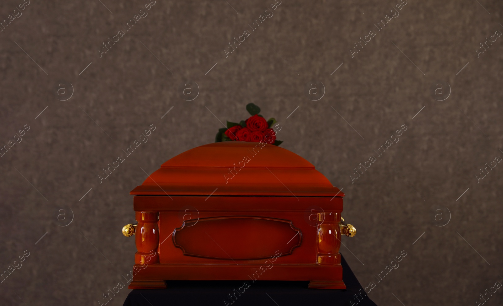 Photo of Wooden funeral casket with red roses at grey wall