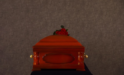 Wooden funeral casket with red roses at grey wall