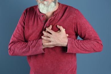 Mature man having heart attack on color background, closeup