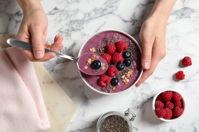 Photo of Woman eating tasty acai smoothie with raspberries and chia seeds at white marble table, top view