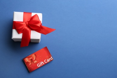 Photo of Gift card and present on blue background, flat lay. Space for text