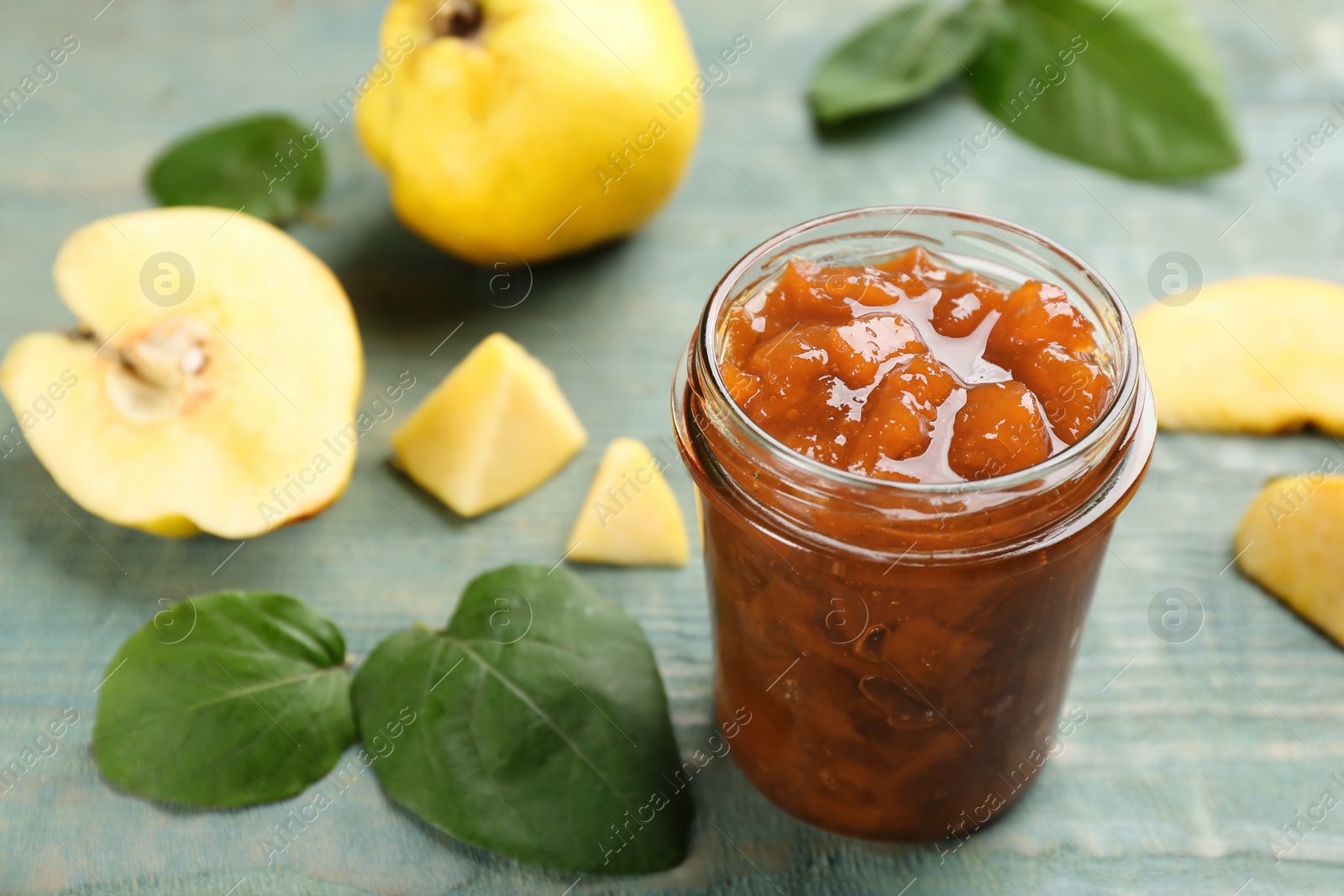 Photo of Delicious quince jam and fruits on blue wooden table. Space for text