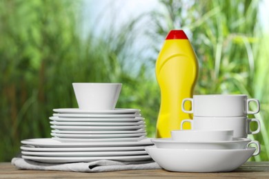 Photo of Set of clean dishware and detergent on white table against blurred background