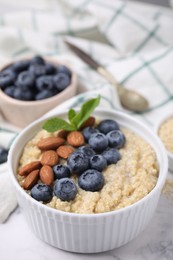 Photo of Bowl of delicious cooked quinoa with almonds and blueberries on white marble table