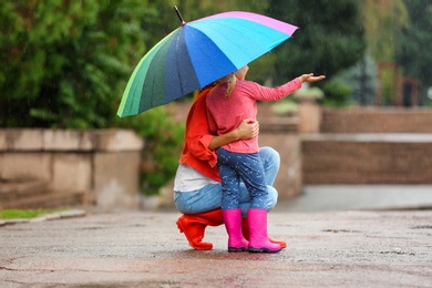 Mother and daughter with bright umbrella under rain outdoors