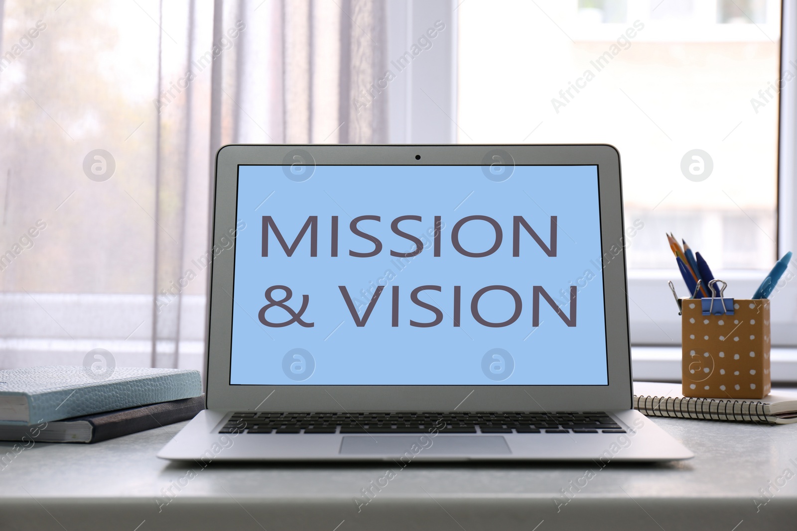Image of Modern laptop with phrase MISSION AND VISION on screen indoors 