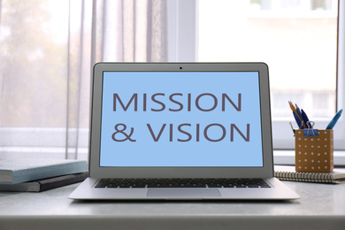 Image of Modern laptop with phrase MISSION AND VISION on screen indoors 