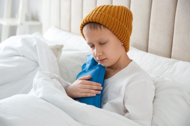 Photo of Ill boy with hot water bottle suffering from cold in bed at home