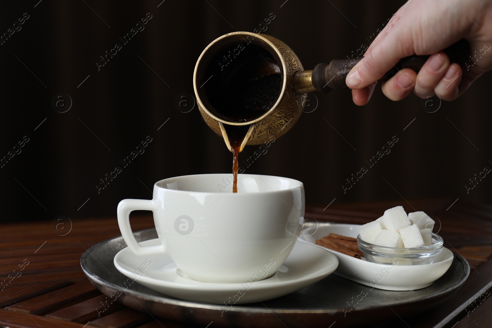 Photo of Turkish coffee. Woman pouring brewed beverage from cezve into cup at wooden table, closeup