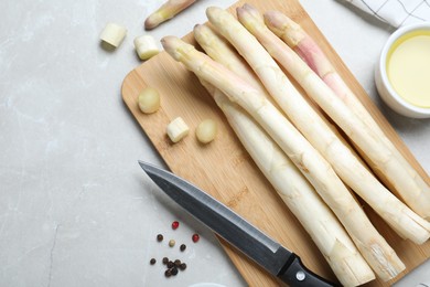 Photo of Fresh white asparagus, knife and cutting board on grey marble table, flat lay