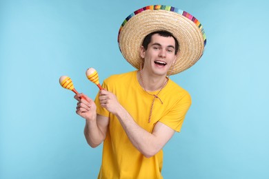 Photo of Young man in Mexican sombrero hat with maracas on light blue background