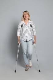 Full length portrait of woman with crutches on grey background