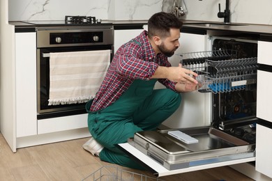 Photo of Serviceman repairing dishwasher cutlery rack in kitchen