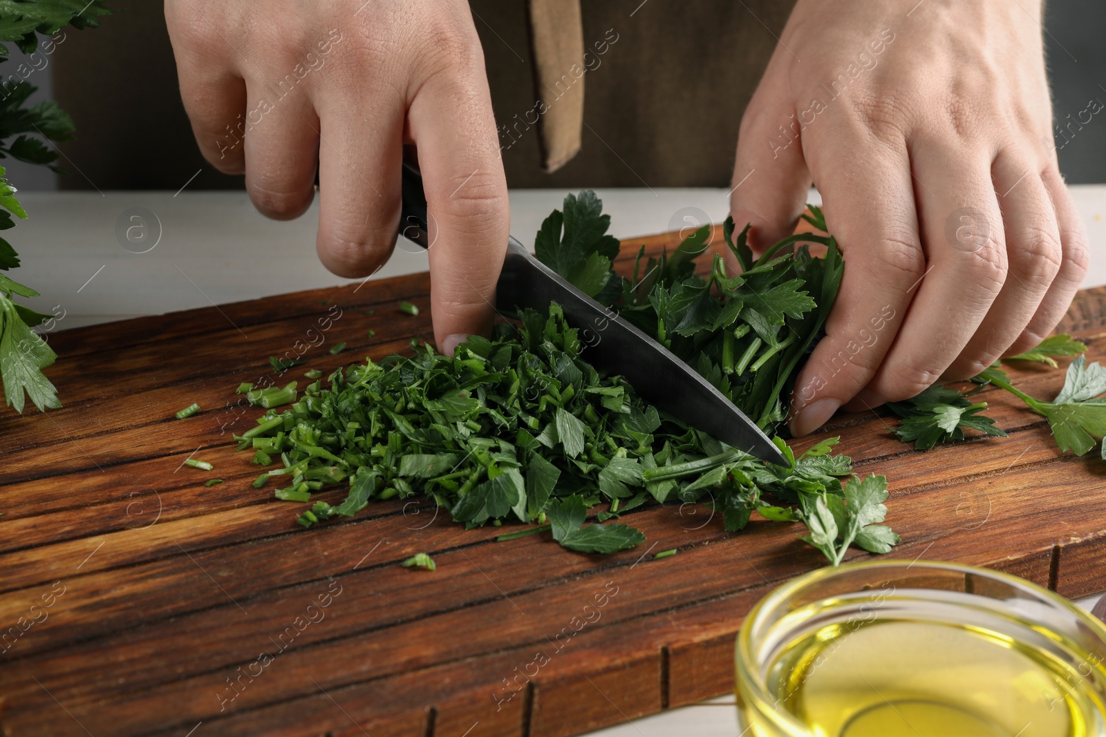 Photo of Woman cutting fresh parsley at white table, closeup