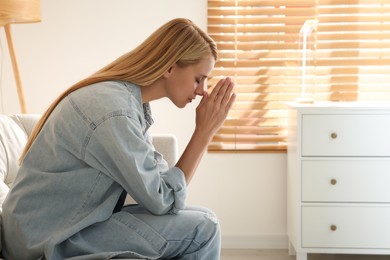 Photo of Religious young woman with clasped hands praying indoors. Space for text