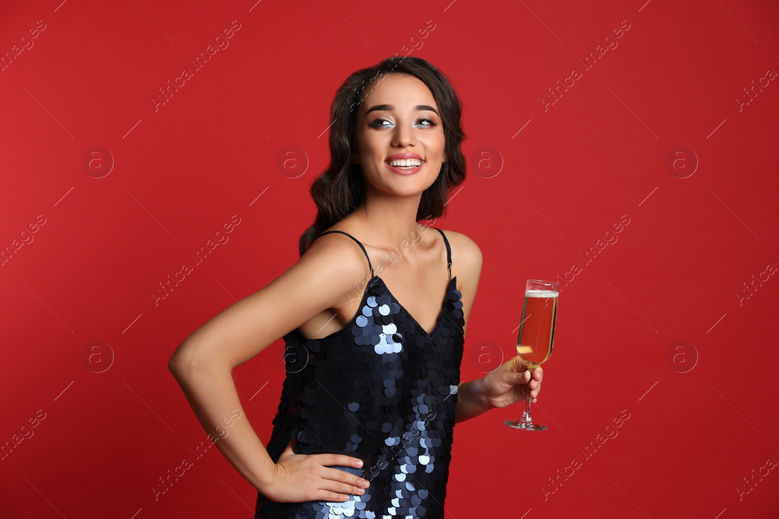 Photo of Beautiful young woman in elegant dress holding glass of champagne on red background. Christmas party