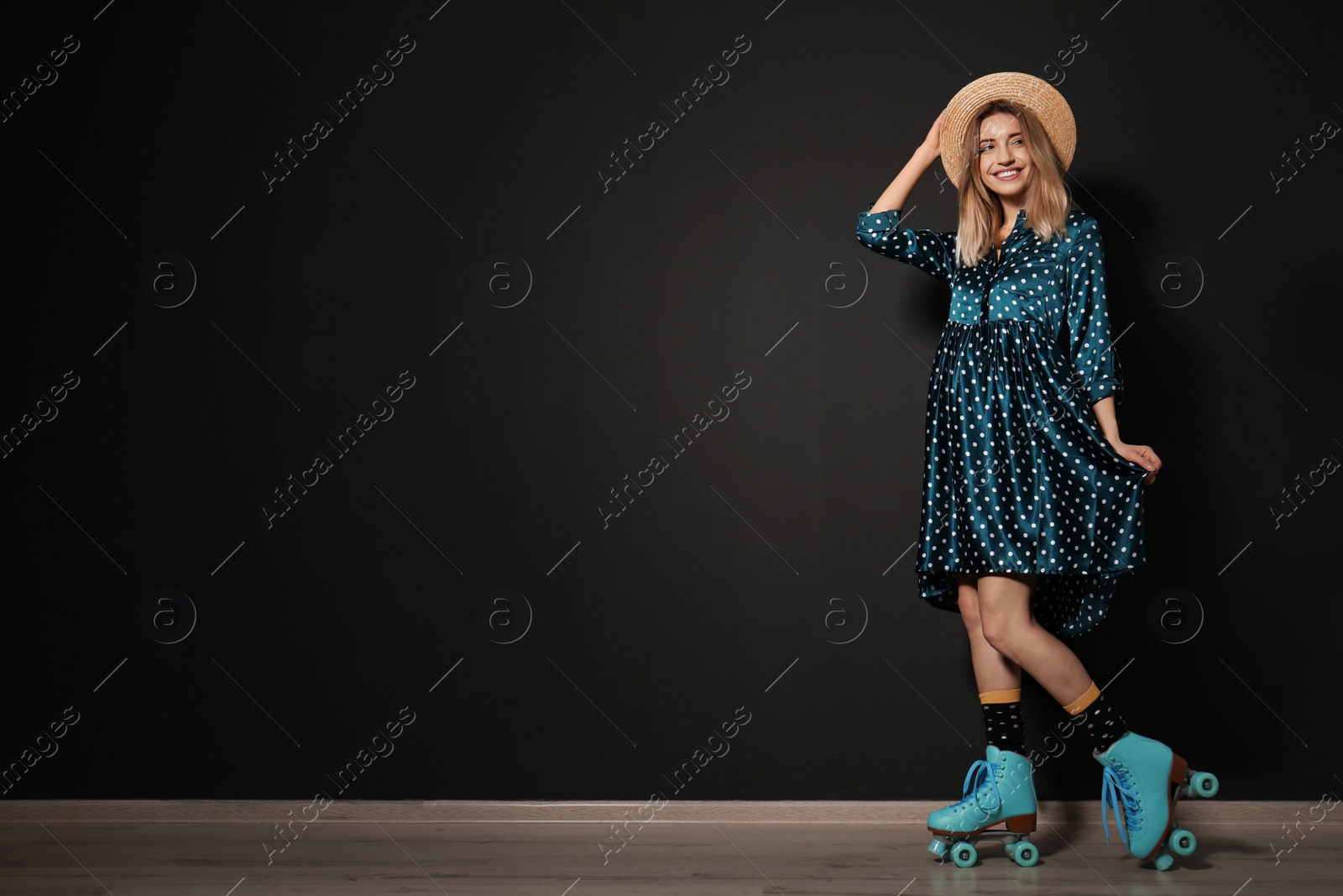 Photo of Young woman with retro roller skates against black wall. Space for text