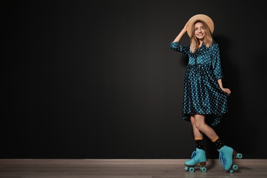 Photo of Young woman with retro roller skates against black wall. Space for text