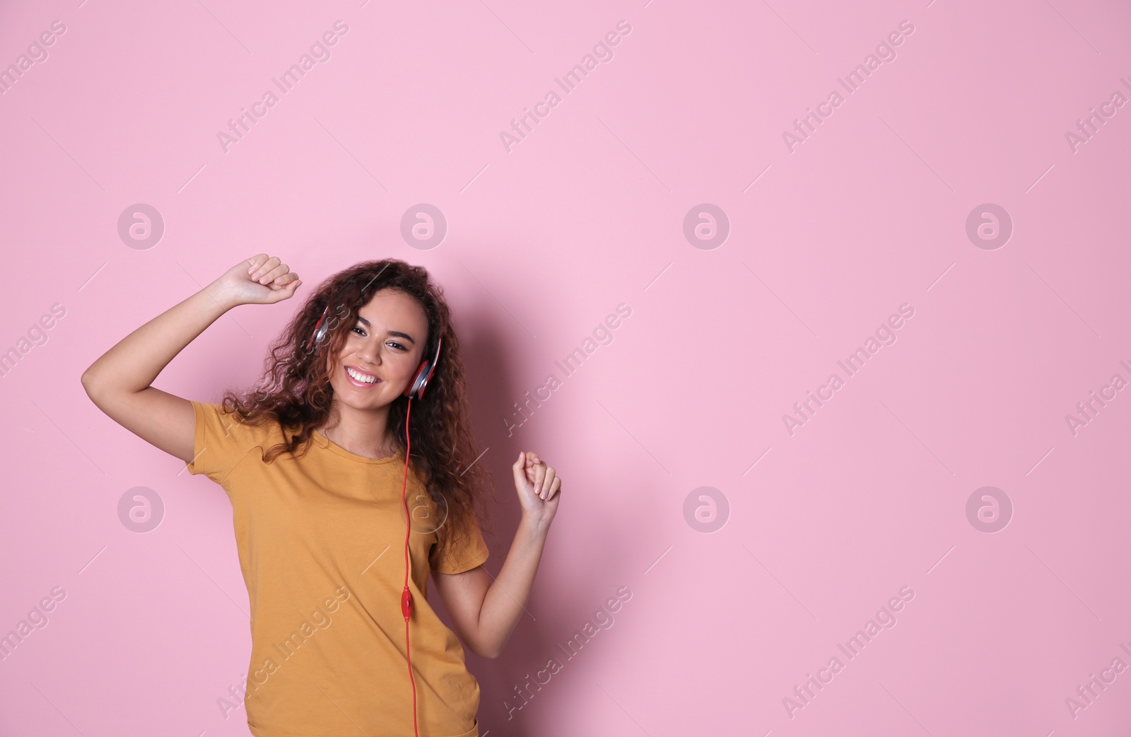 Photo of African-American girl listening to music with headphones on color background, space for text