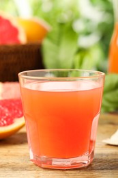 Photo of Glass of delicious grapefruit juice on wooden table against blurred background, space for text