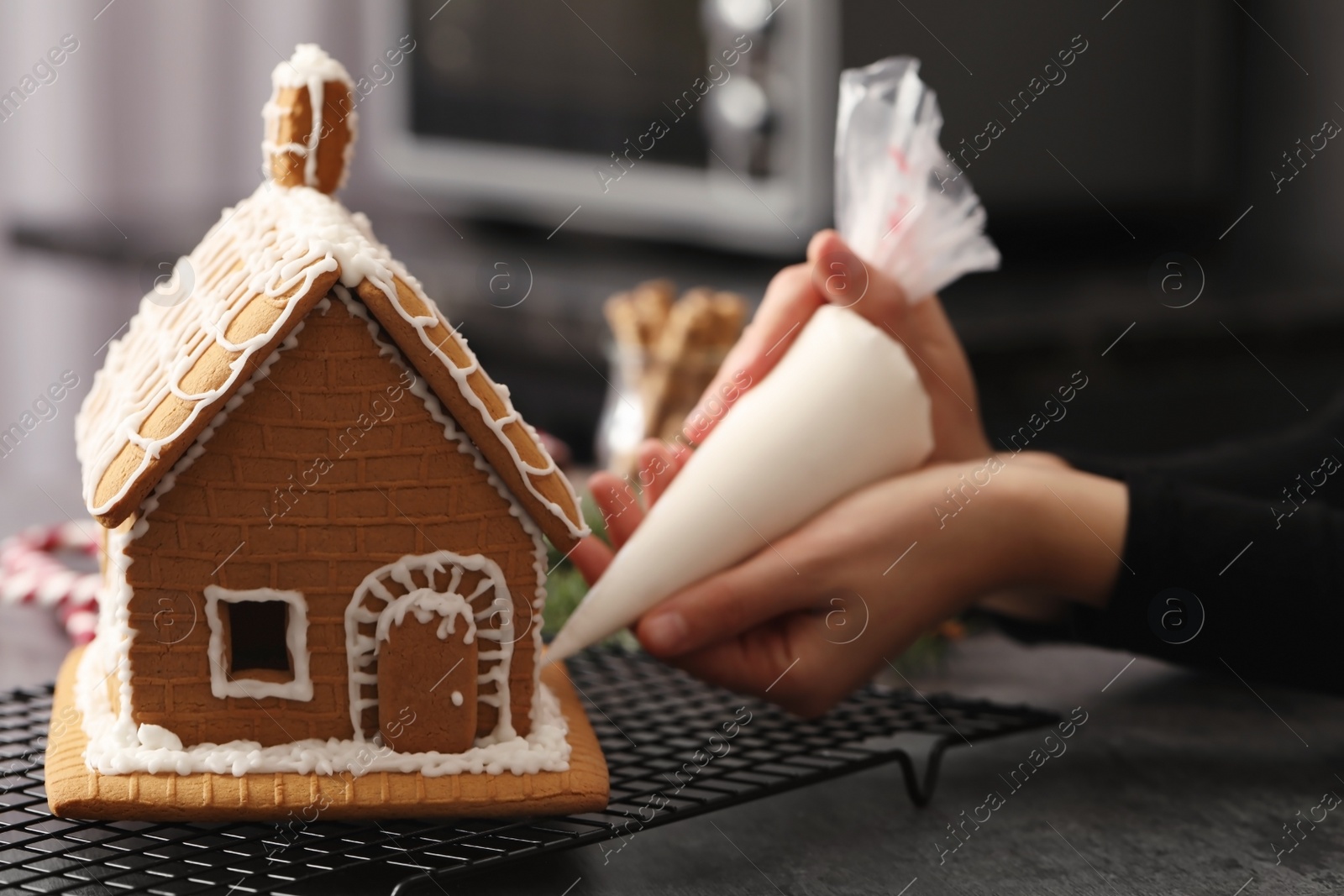 Photo of Woman decorating gingerbread house with icing at grey table, closeup