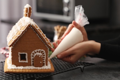 Photo of Woman decorating gingerbread house with icing at grey table, closeup