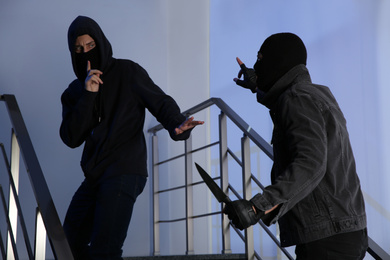 Photo of Men in masks with knife on stairs indoors. Dangerous criminals