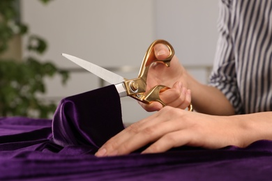 Photo of Woman cutting fabric with sharp scissors at wooden table indoors, closeup