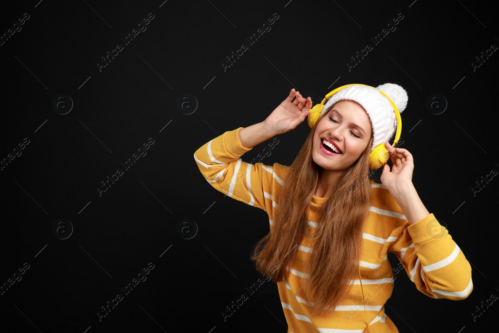 Photo of Young woman listening to music with headphones on black background, space for text