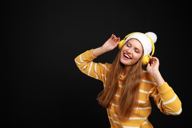 Young woman listening to music with headphones on black background, space for text