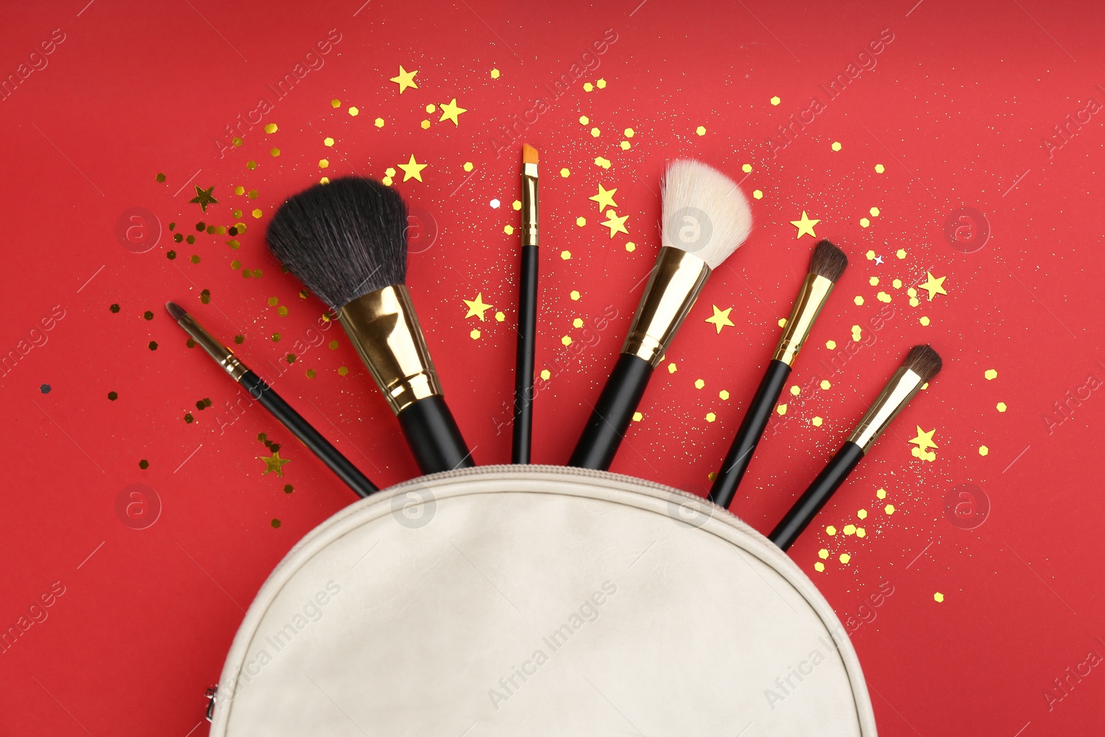 Photo of Different makeup brushes, case and shiny confetti on red background, flat lay