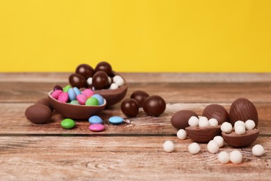 Photo of Delicious chocolate eggs and candies on wooden table against yellow background