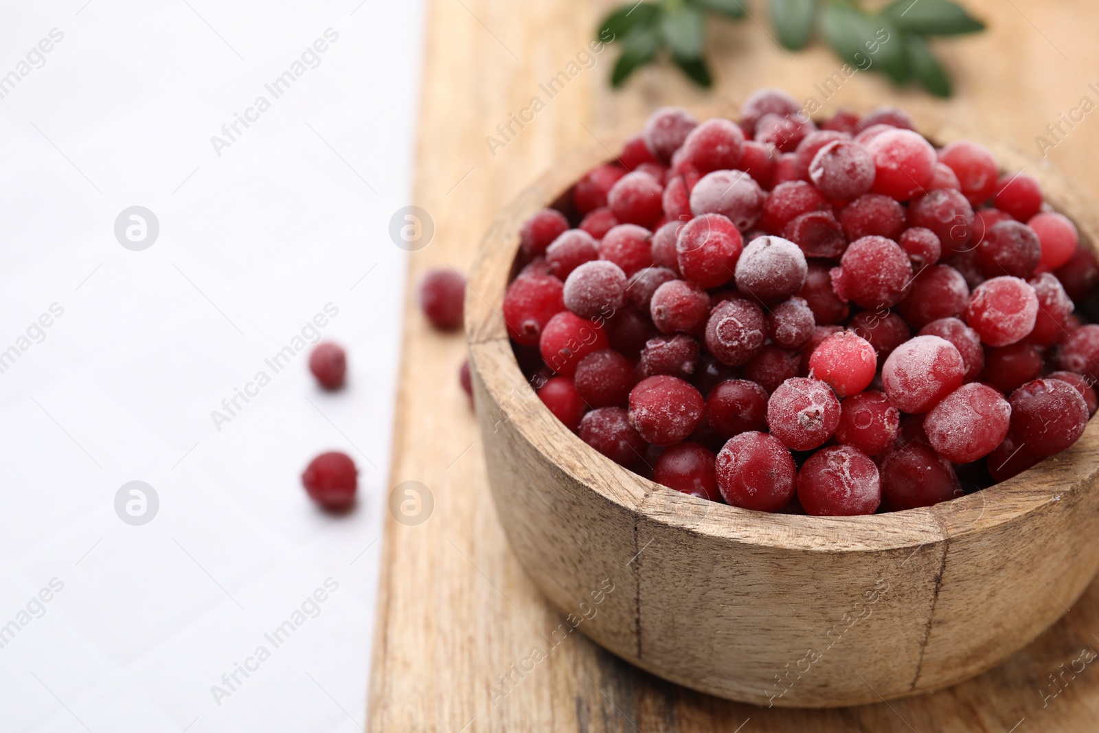 Photo of Frozen red cranberries in bowl on white table, closeup. Space for text