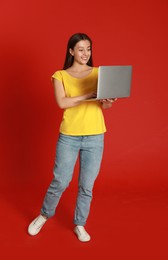 Photo of Young woman with modern laptop on red background