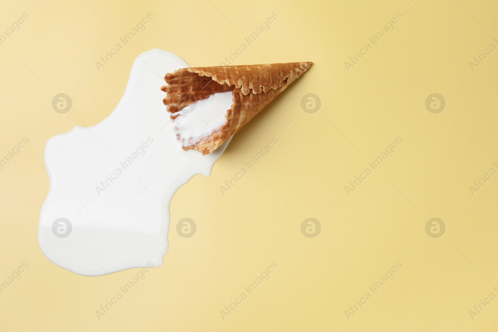 Photo of Melted ice cream and wafer cone on beige background, top view. Space for text