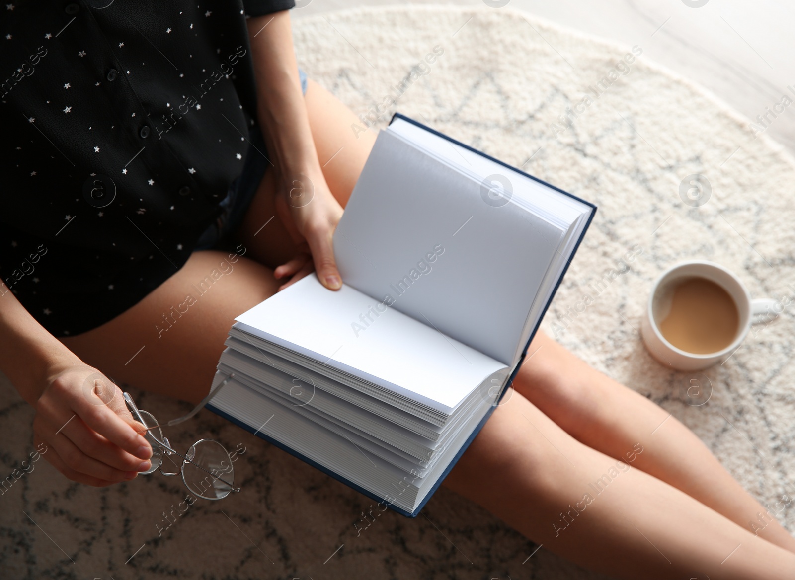 Photo of Young woman with cup of coffee reading book on floor at home, above view