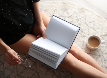 Photo of Young woman with cup of coffee reading book on floor at home, above view