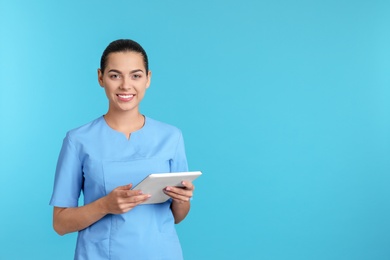 Portrait of young medical assistant with tablet on color background. Space for text
