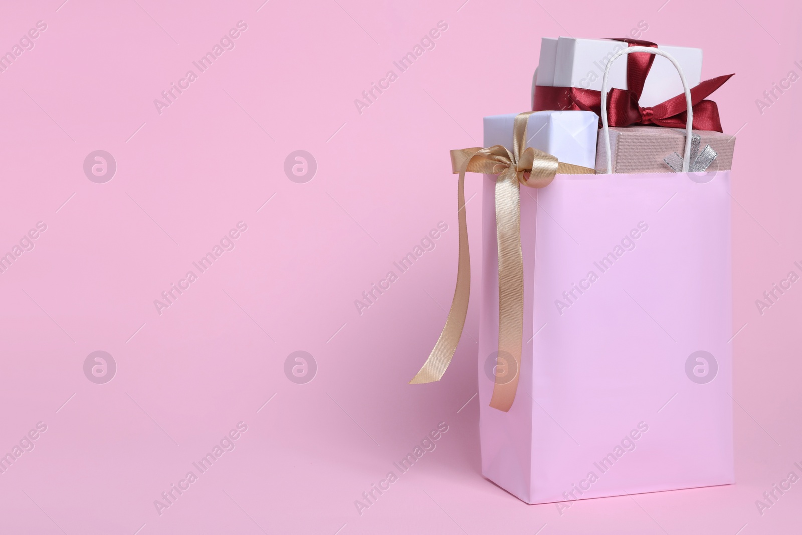 Photo of Color paper shopping bag full of gift boxes on pink background. Space for text
