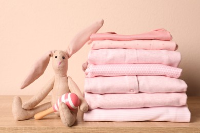 Stack of baby girl's clothes, rattle and toy bunny on wooden table