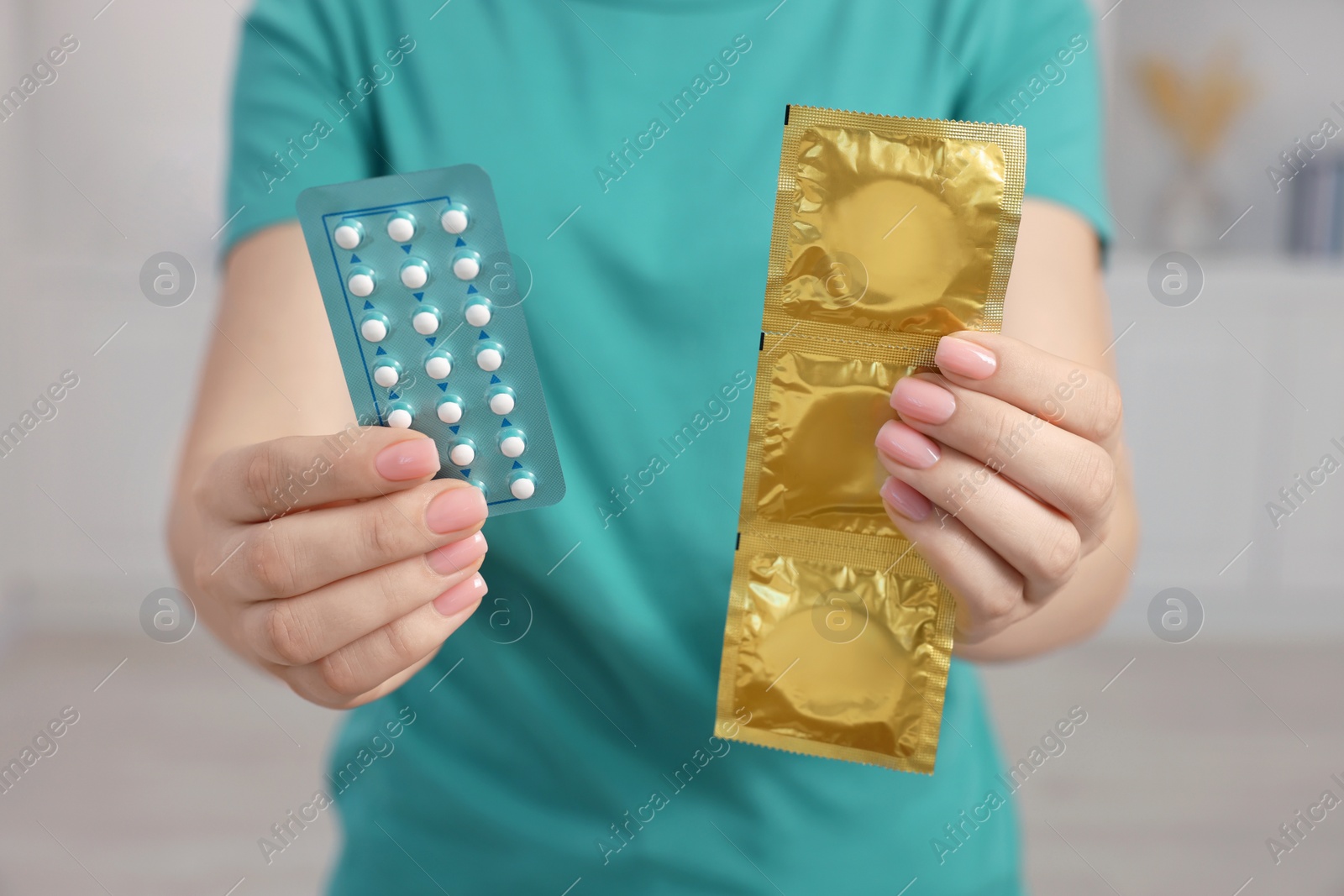 Photo of Woman holding condoms and contraceptive pills on blurred background, closeup. Choosing birth control method