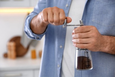Photo of Man using manual coffee grinder in kitchen, closeup
