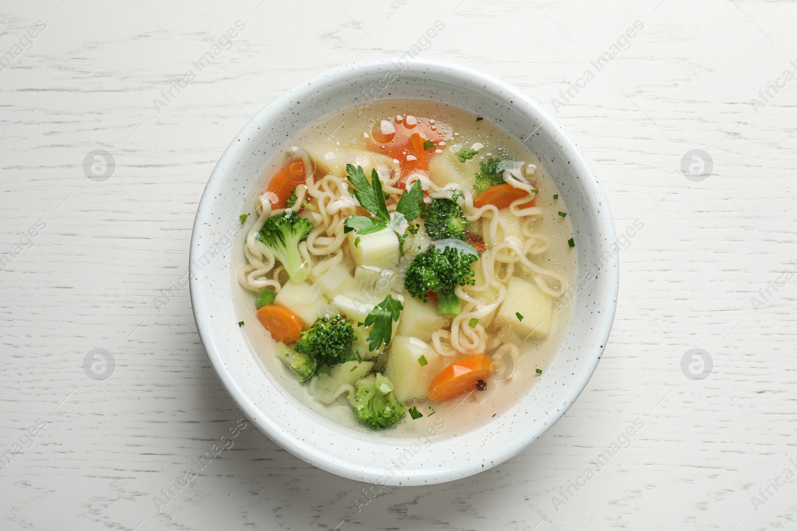 Photo of Bowl of fresh homemade vegetable soup on white wooden background, top view