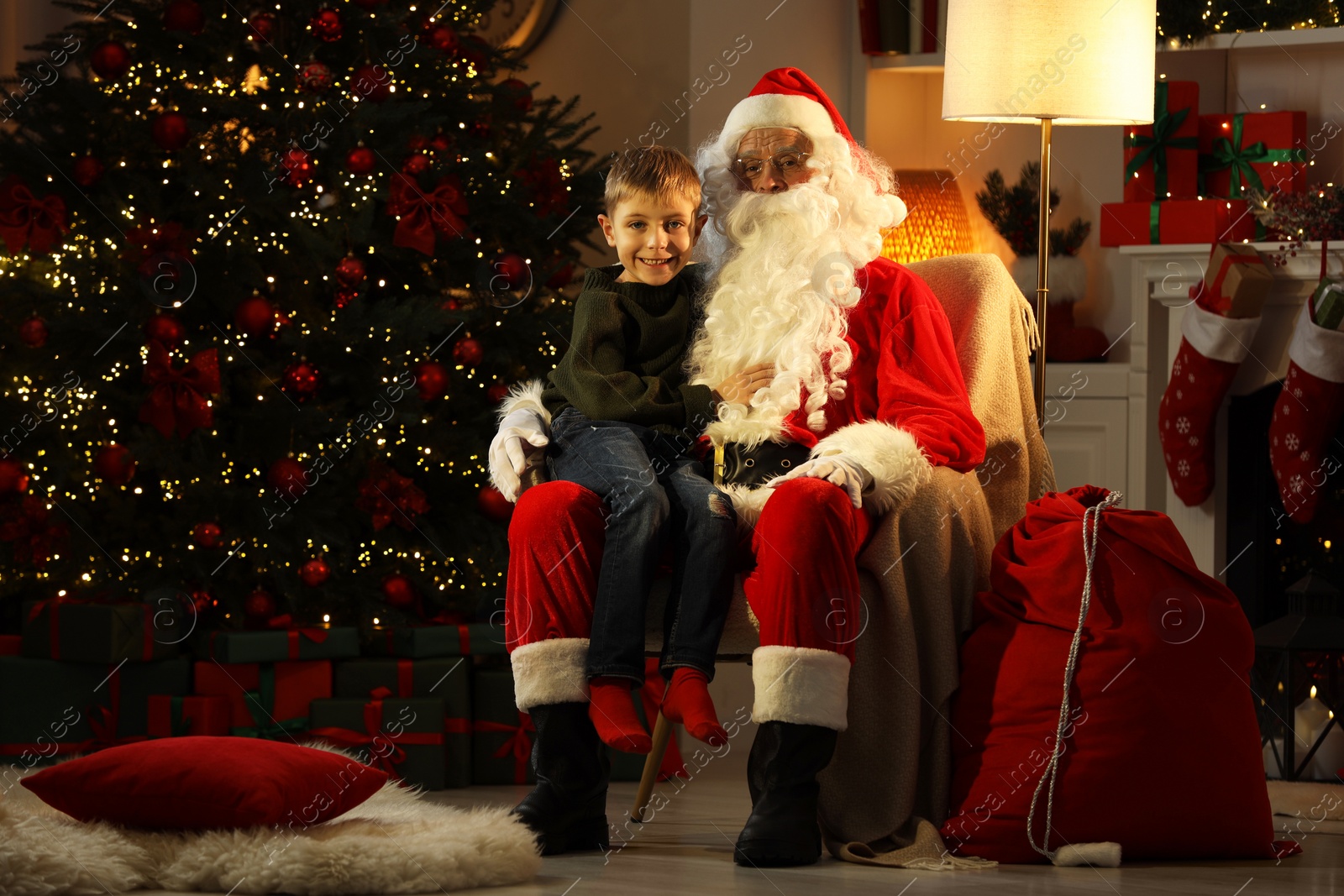 Photo of Merry Christmas. Little boy sitting on Santa's knee at home