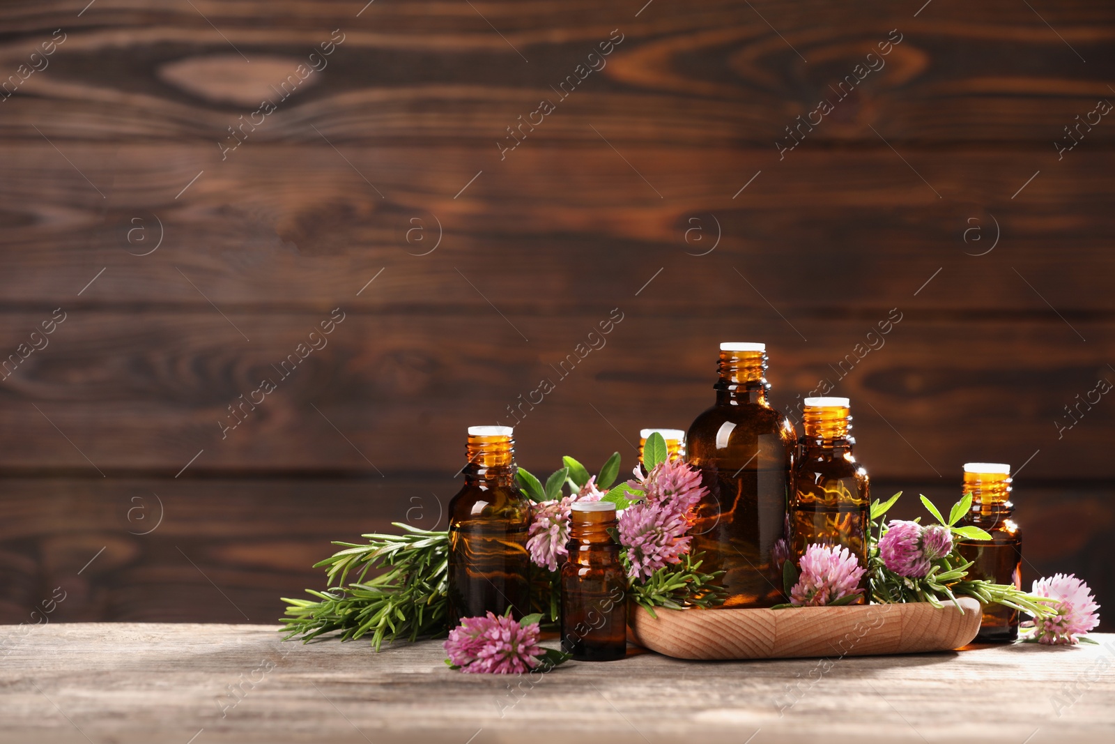 Photo of Bottles with essential oils, clover and rosemary on wooden table. Space for text