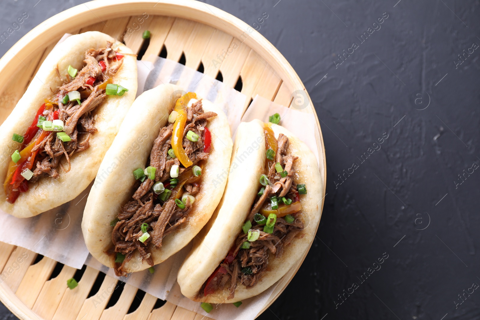 Photo of Delicious gua bao in bamboo steamer on black table, top view. Space for text