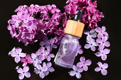 Photo of Bottle with essential oil, lilac flowers and water on black surface, flat lay